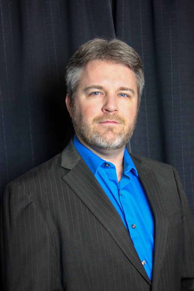 Professional headshot of Phil Andreas in a blue shirt and pinstripe suit